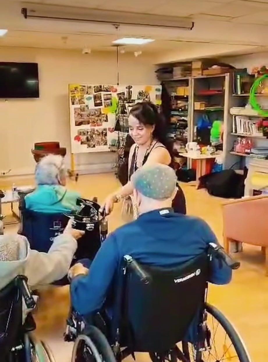 Une intervenante danse avec des résidents en fauteuil roulant dans une salle d'activités