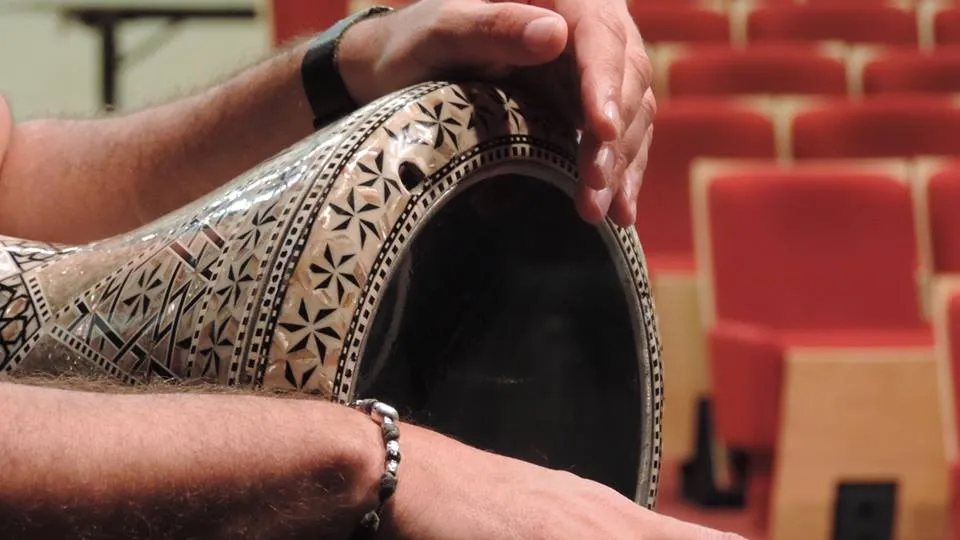 Gros plan sur une darbouka ornée de nacre entre les mains d'un percussionniste